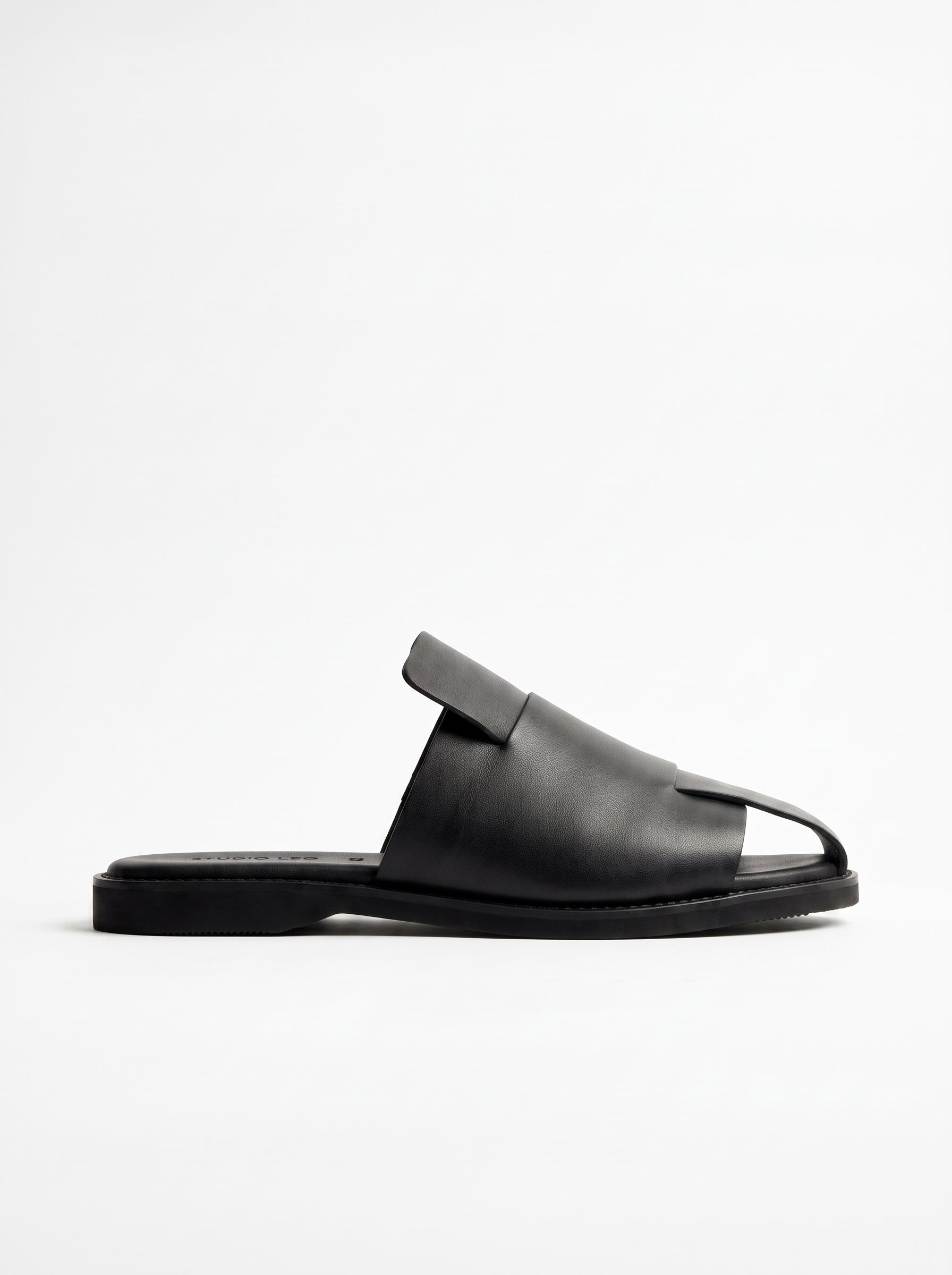 A single black leather slide sandal with a wide strap and a small decorative tab on the instep, shown in profile against a plain white background.